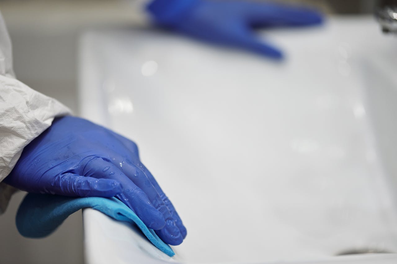 Close-up of a person sanitizing a bathroom sink with gloves and cloth, focusing on hygiene and cleanliness.