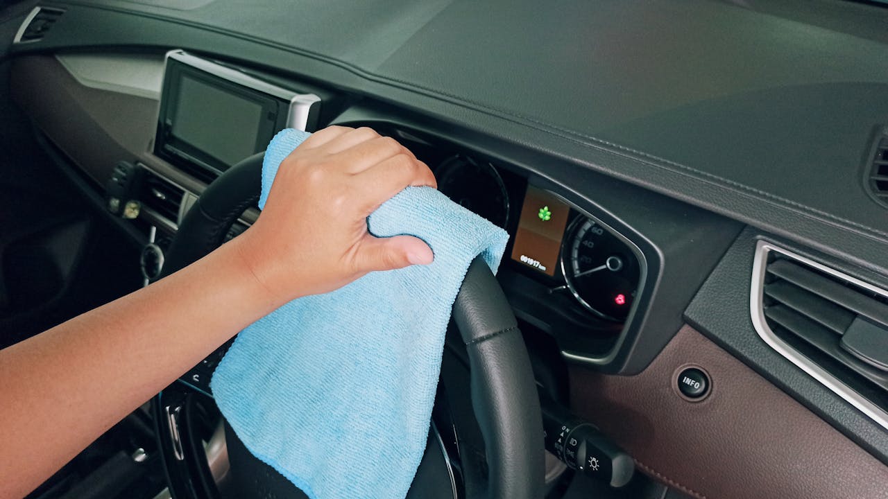 Close-up of a hand wiping a car steering wheel with a microfiber cloth for cleanliness.